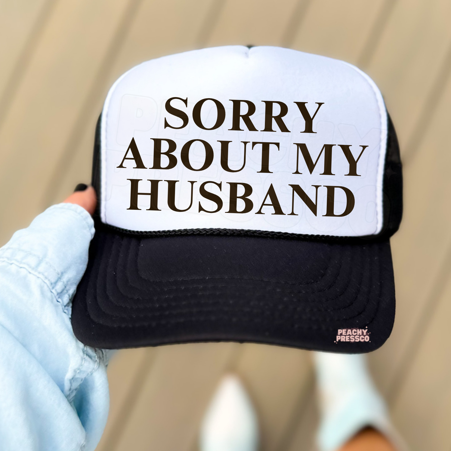 Black and white trucker hat with “Sorry About My Husband” text graphic.