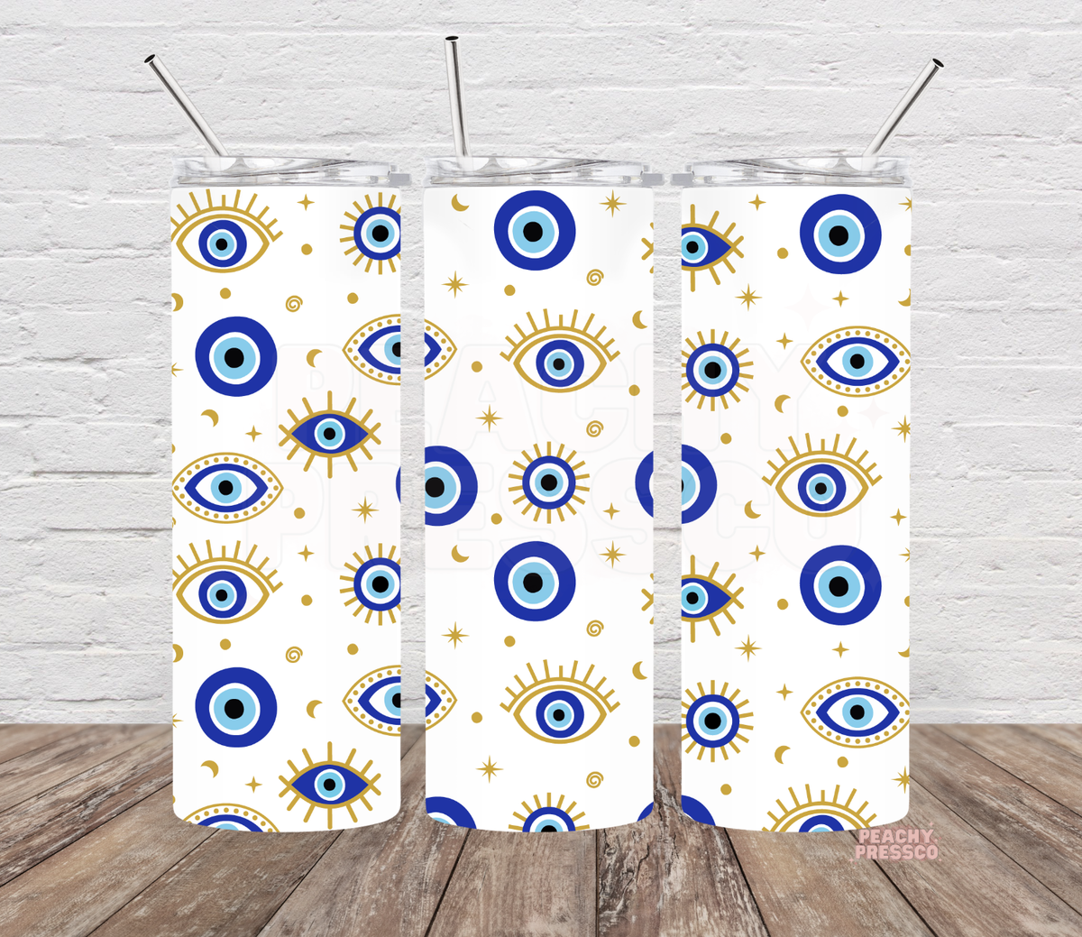 Three views of a white skinny tumbler with blue evil eye symbols, gold sunbursts, crescent moons and stars, clear lids and metal straws.