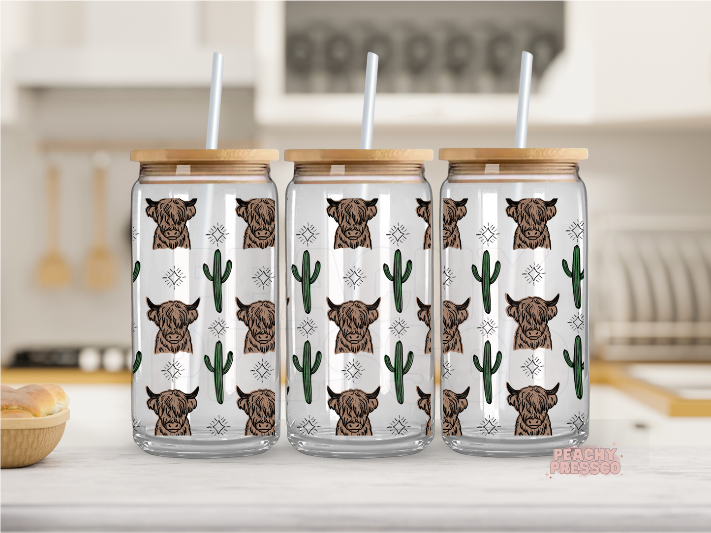 Glass cup with bamboo lids and straws, featuring illustrations of highland cows and cacti, displayed in a kitchen setting.