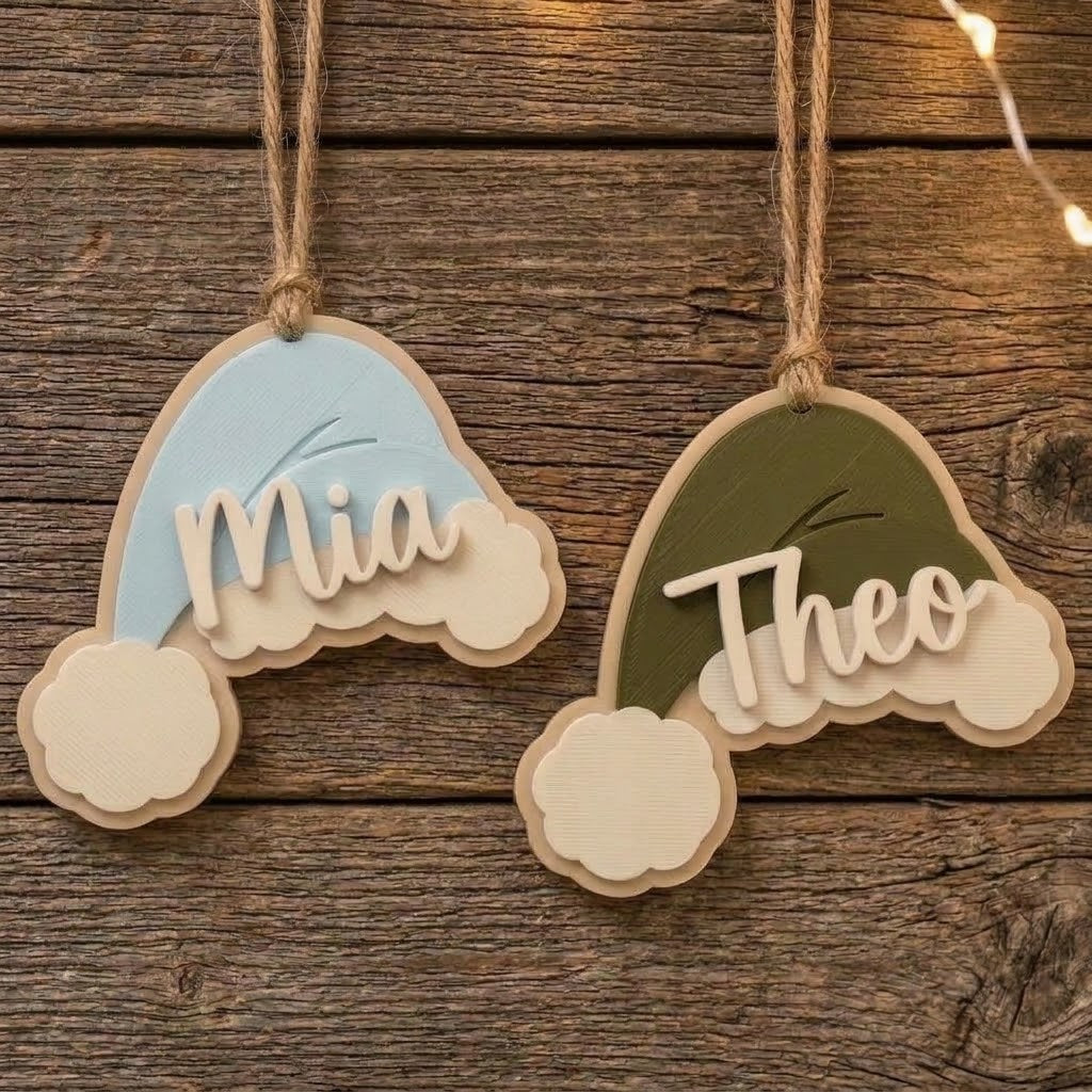 Light blue and green personalized Santa hat Christmas ornaments hanging on a rustic wooden background with the names Mia and Theo