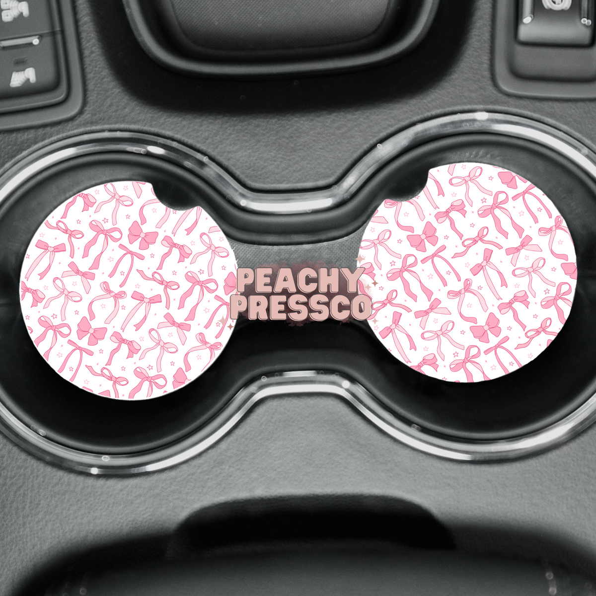 Pink bow car coasters with a white and pink ribbon pattern displayed in vehicle cup holders.