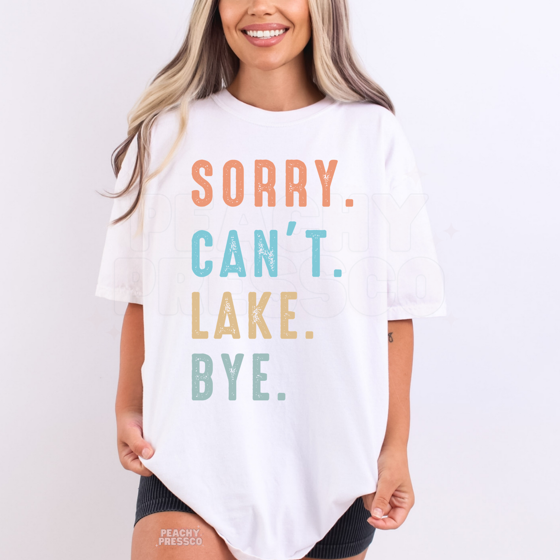Woman wearing oversized white Sorry Can’t Lake Bye graphic t-shirt with colorful pastel text.