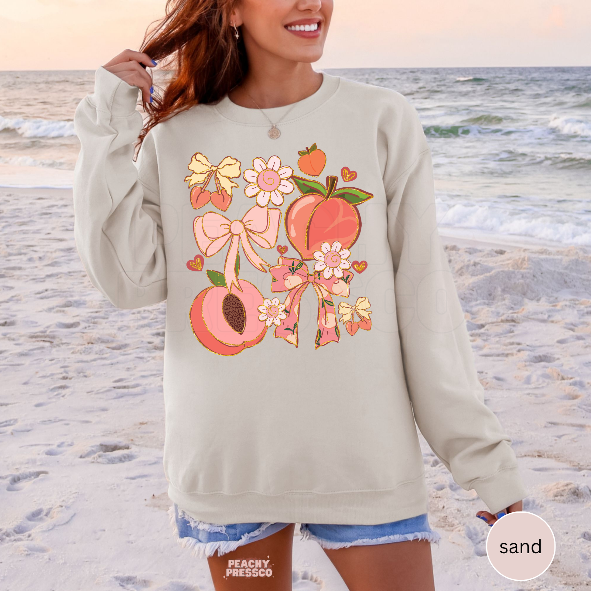 Woman wearing a sand colored beach sweatshirt with cute peach, bow, and daisy graphic in soft pastel tones.