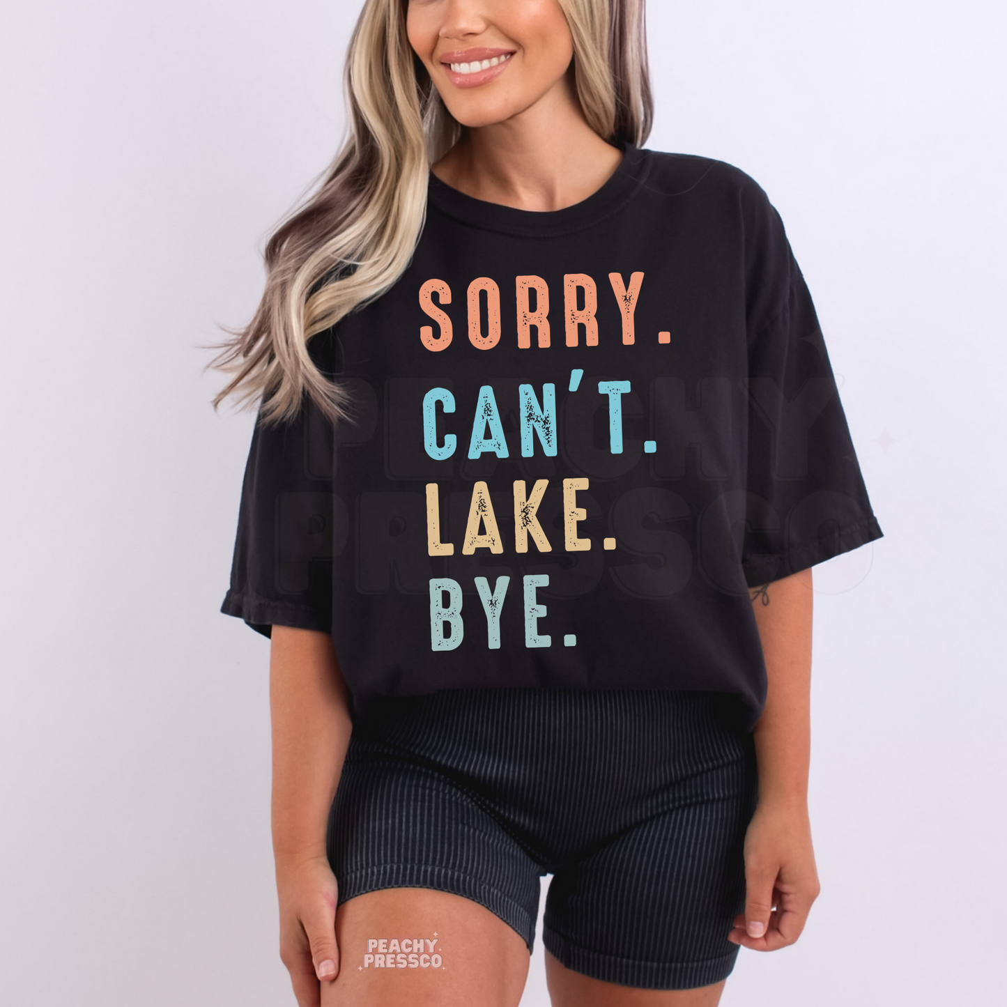Woman wearing oversized black graphic t-shirt with distressed pastel “Sorry. Can’t. Lake. Bye.” lake themed design.