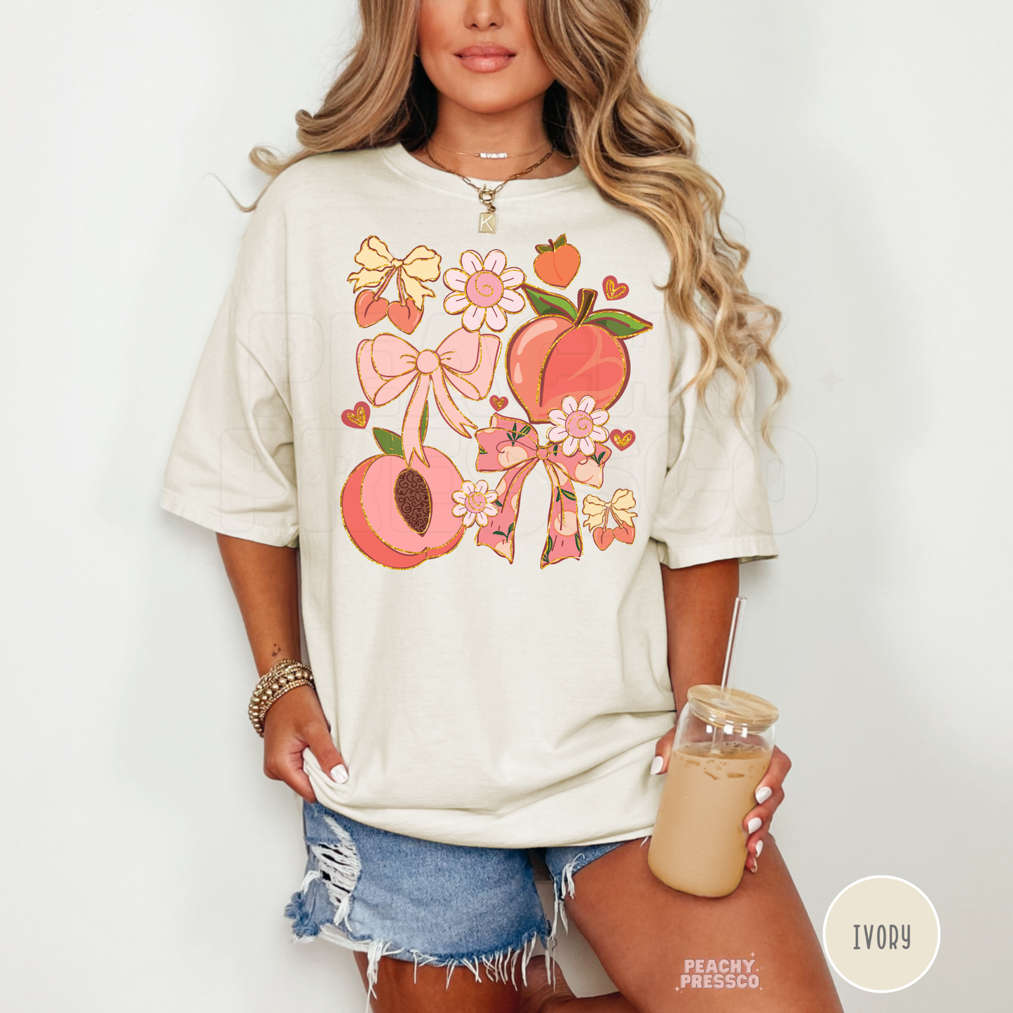 Woman wearing an ivory oversized graphic t-shirt featuring peaches, bows, cherries, and floral coquette-inspired artwork.