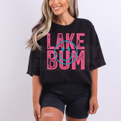 Woman wearing oversized black Lake Bum graphic t-shirt with distressed pink lettering and blue smiley face design.