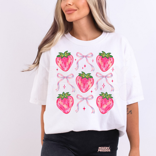 Woman wearing a white oversized t-shirt with cute pink strawberries, bows, and sparkles in a coquette aesthetic graphic print.