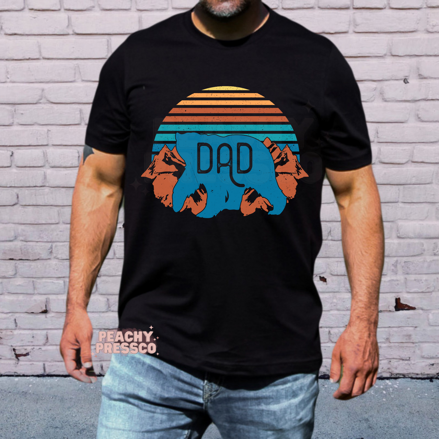 Man wearing black t-shirt with vintage bear “Dad” graphic featuring retro sunset stripes and mountain design.