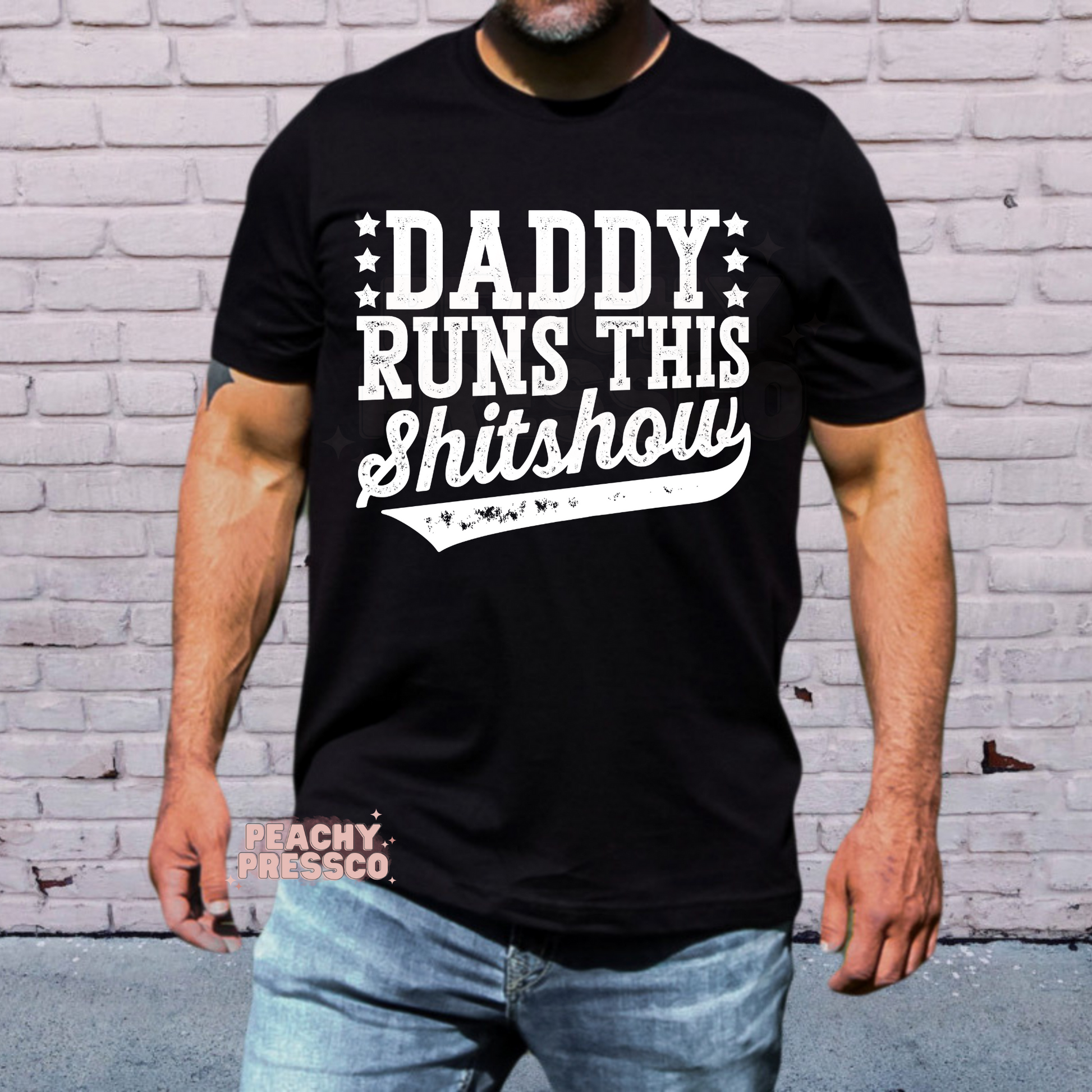 Man modeling black t-shirt featuring bold white “Daddy Runs This Shitshow” slogan design with vintage distressed style.