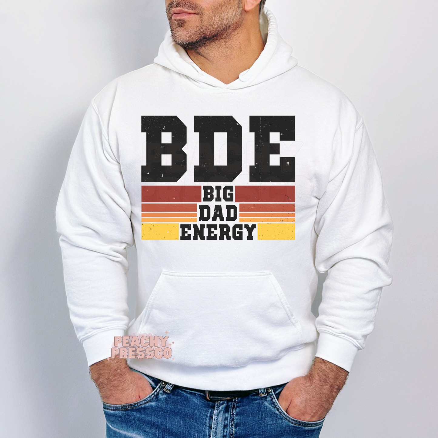Man modeling white hoodie with retro “BDE Big Dad Energy” graphic and distressed sunset stripe print.