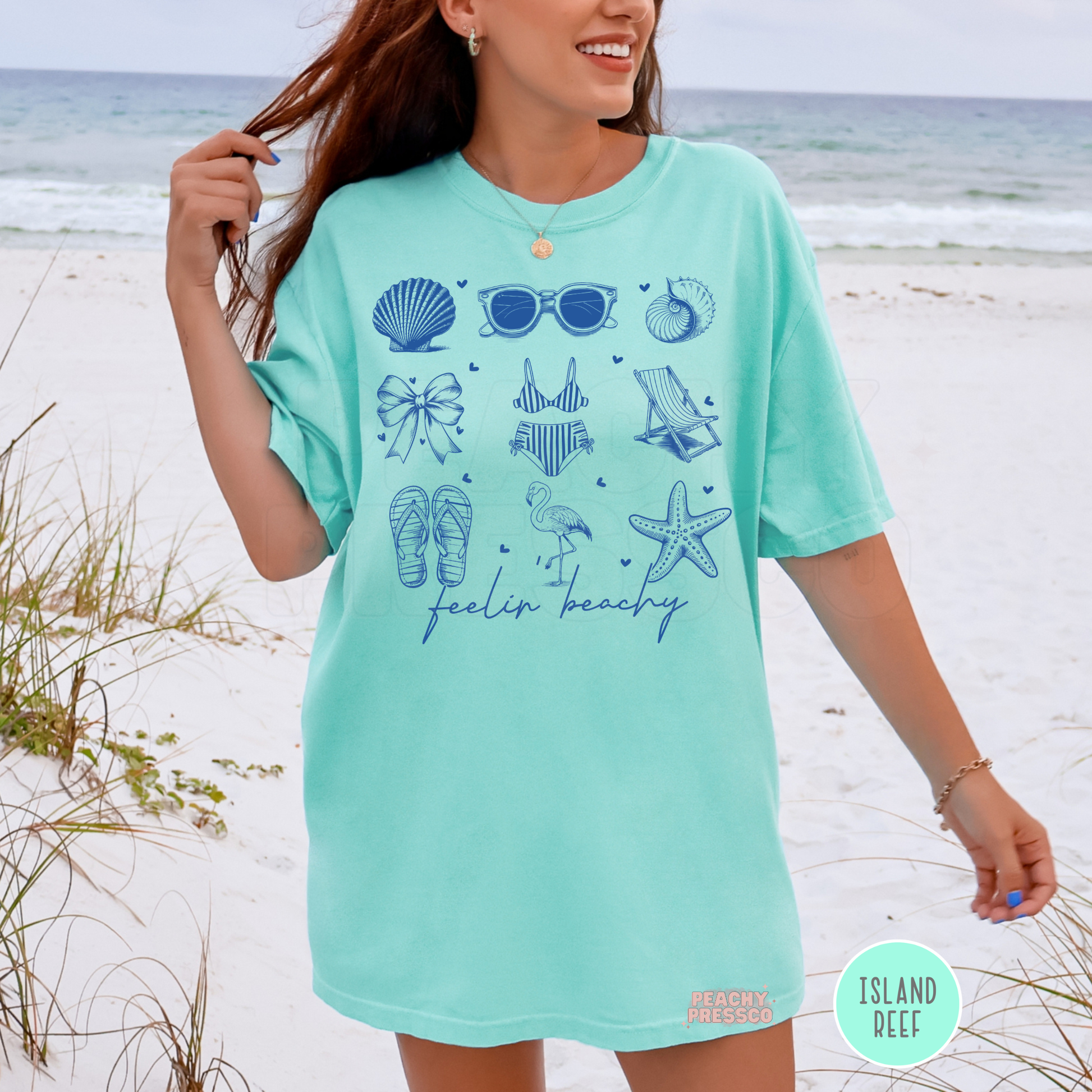 Woman wearing an island reef oversized t-shirt with blue beach themed doodle graphics including shells, bikini, beach chair, and starfish design.