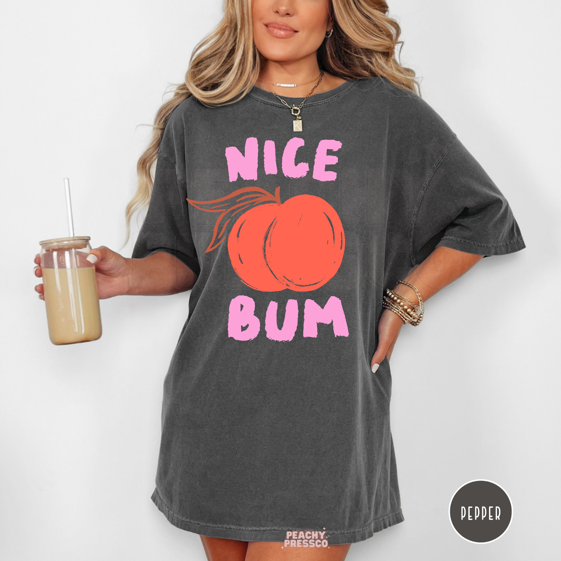 Woman wearing a pepper gray oversized graphic t-shirt with a peach illustration and pink “Nice Bum” text in a fun retro style.