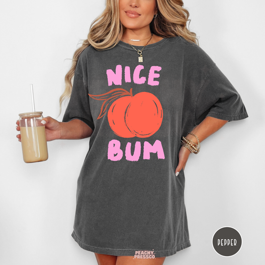 Woman wearing a pepper gray oversized graphic t-shirt with a peach illustration and pink “Nice Bum” text in a fun retro style.