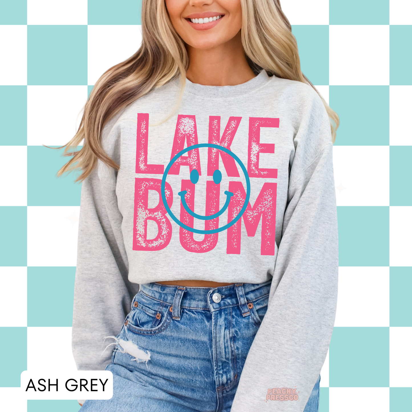 Woman wearing ash grey Lake Bum sweatshirt with pink distressed lettering and blue smiley face graphic.