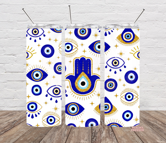20 oz white skinny tumbler featuring royal blue evil eyes, gold stars, celestial accents and a large blue Hamsa hand with an eye in the center.