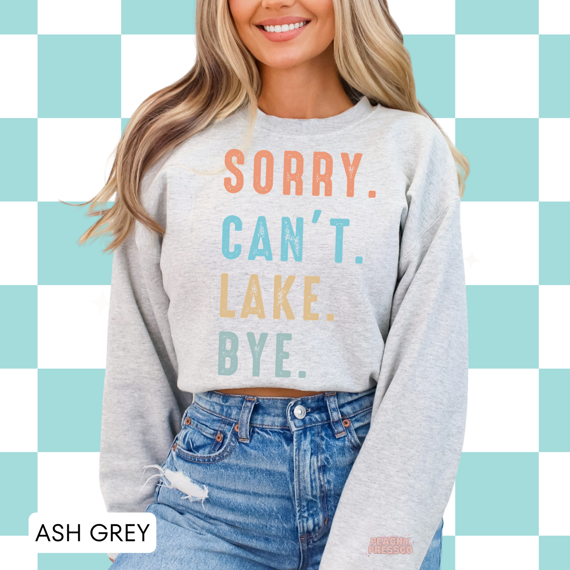 Woman wearing ash grey crewneck sweatshirt with colorful “Sorry. Can’t. Lake. Bye.” retro lake life graphic.