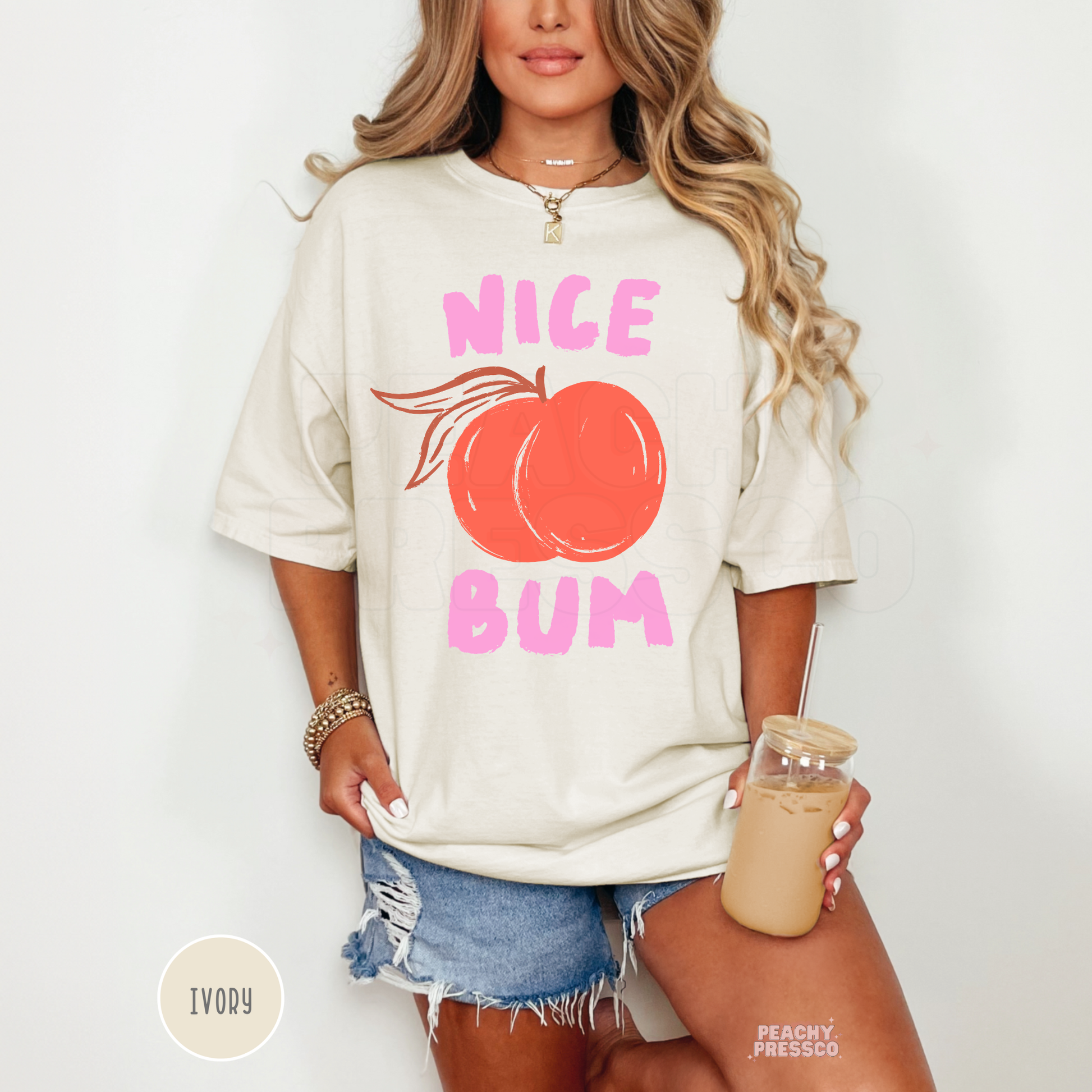 Woman wearing an ivory oversized t-shirt featuring a peach graphic with pink “Nice Bum” lettering and a playful summer aesthetic.