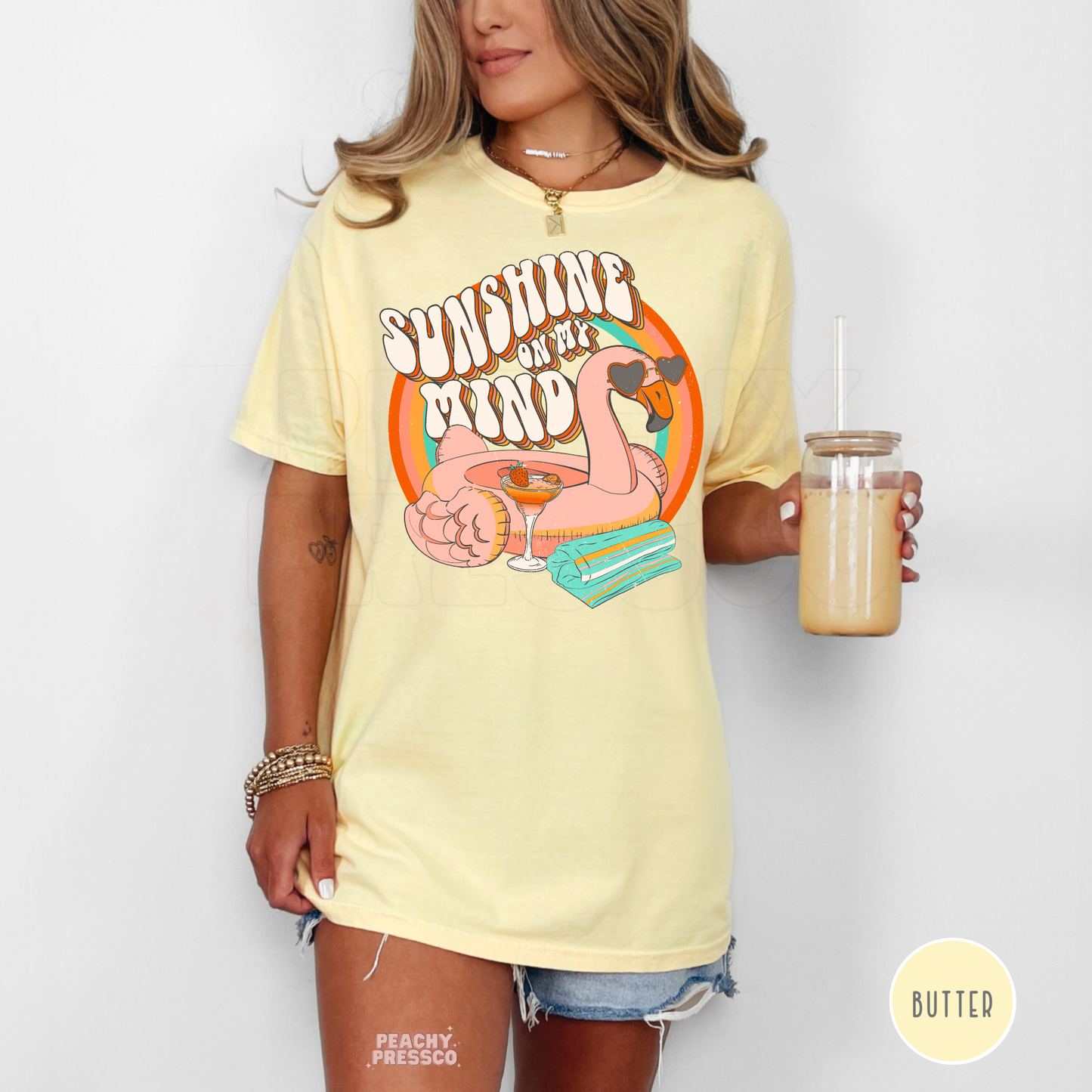 Woman wearing a butter yellow oversized graphic t-shirt featuring a retro “Sunshine on My Mind” flamingo float design with rainbow and tropical drink artwork.
