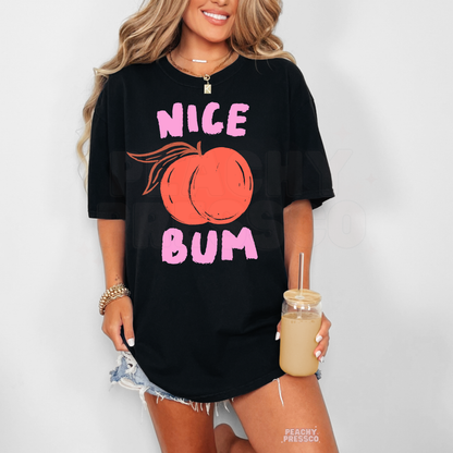 Woman wearing a black oversized graphic tee with pink “Nice Bum” text and a peach illustration in a bold retro design.