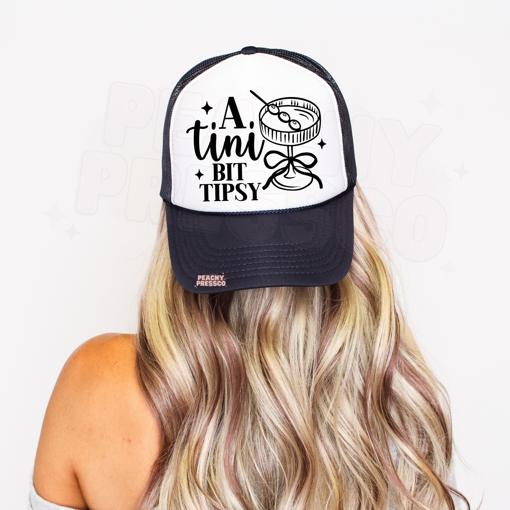 White and navy trucker hat featuring “A Tiny Bit Tipsy” with cocktail illustration.
