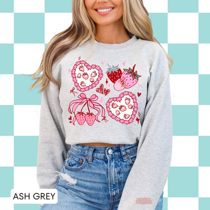 Woman wearing ash grey crewneck sweatshirt with cute pink strawberry hearts, bows, and coquette-inspired graphic design.