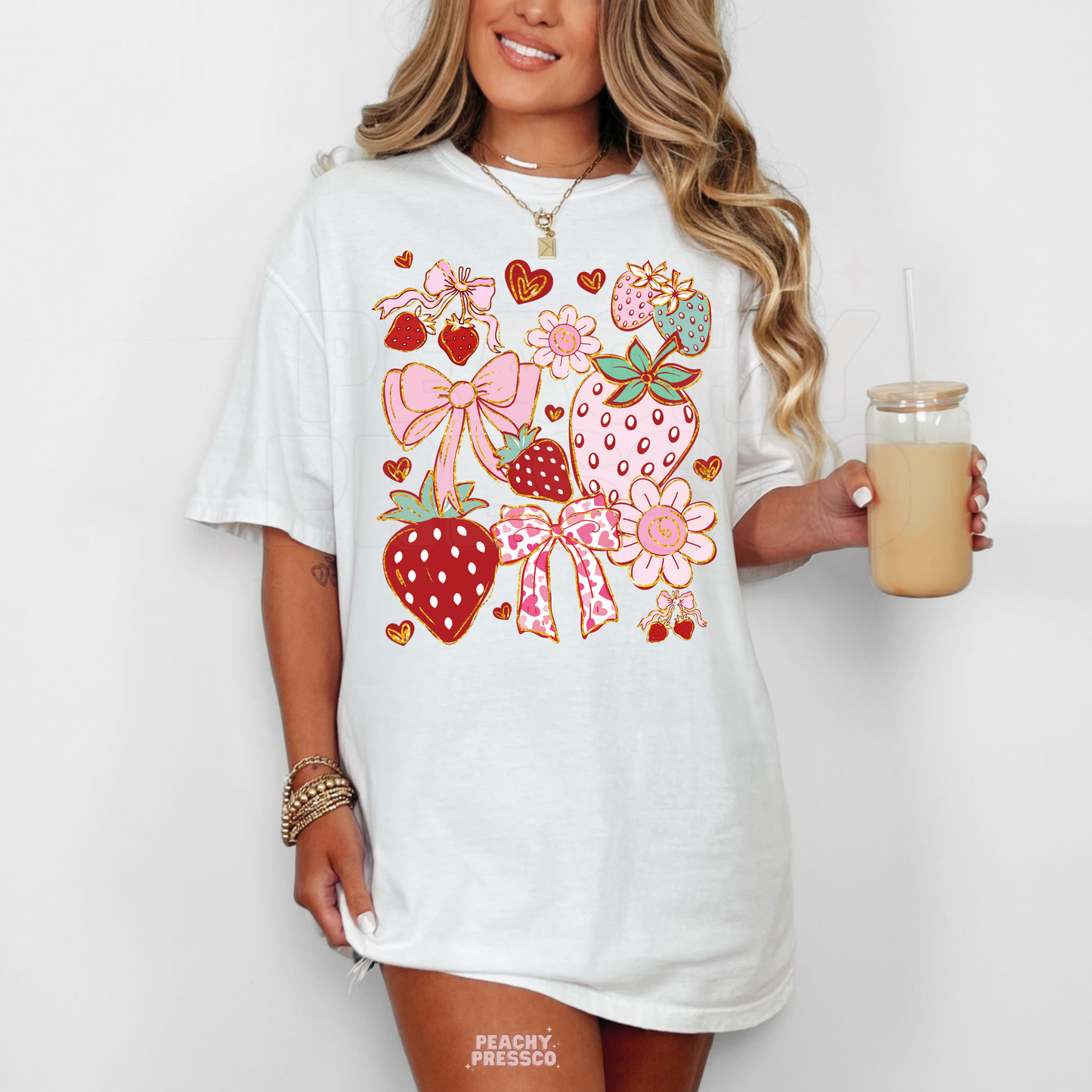Woman wearing a white oversized t-shirt dress with a playful strawberry and bow collage graphic in pink, red, and pastel tones.