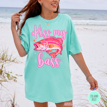 Woman wearing an island reef oversized graphic t-shirt featuring a vibrant bass fish illustration with “Kiss My Bass” saying at the beach for summer and lake life style.