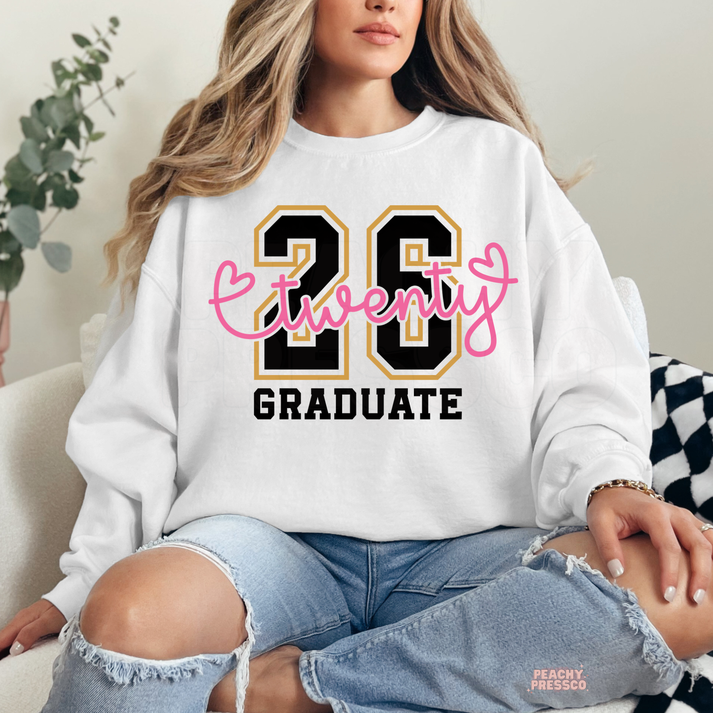 Woman wearing white sweatshirt featuring Twenty 26 Graduate design with pink script lettering and Class of 2026 graphic.