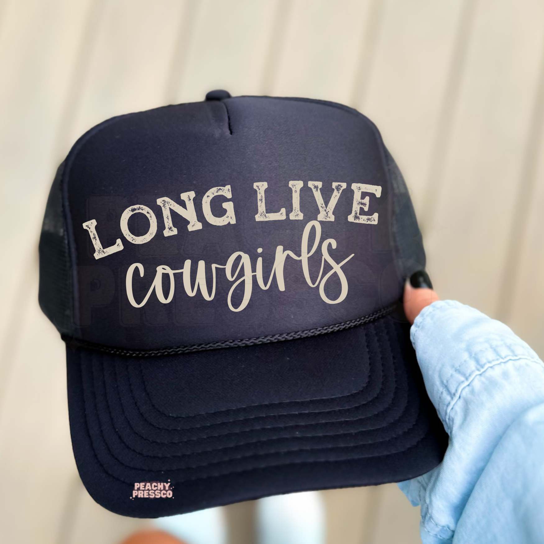 Black trucker hat with “Long Live Cowgirls” western graphic held outdoors. Trendy women’s cowboy hat for country concerts, rodeos and western style.