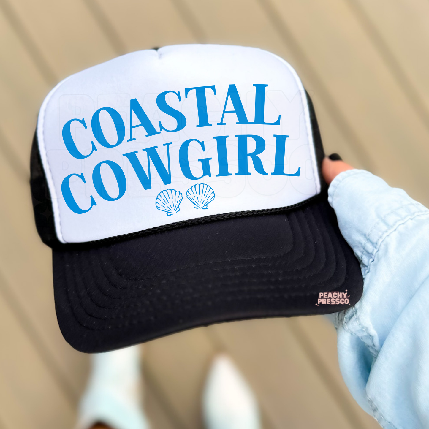Black and white trucker hat with Coastal Cowgirl text and shell icons.
