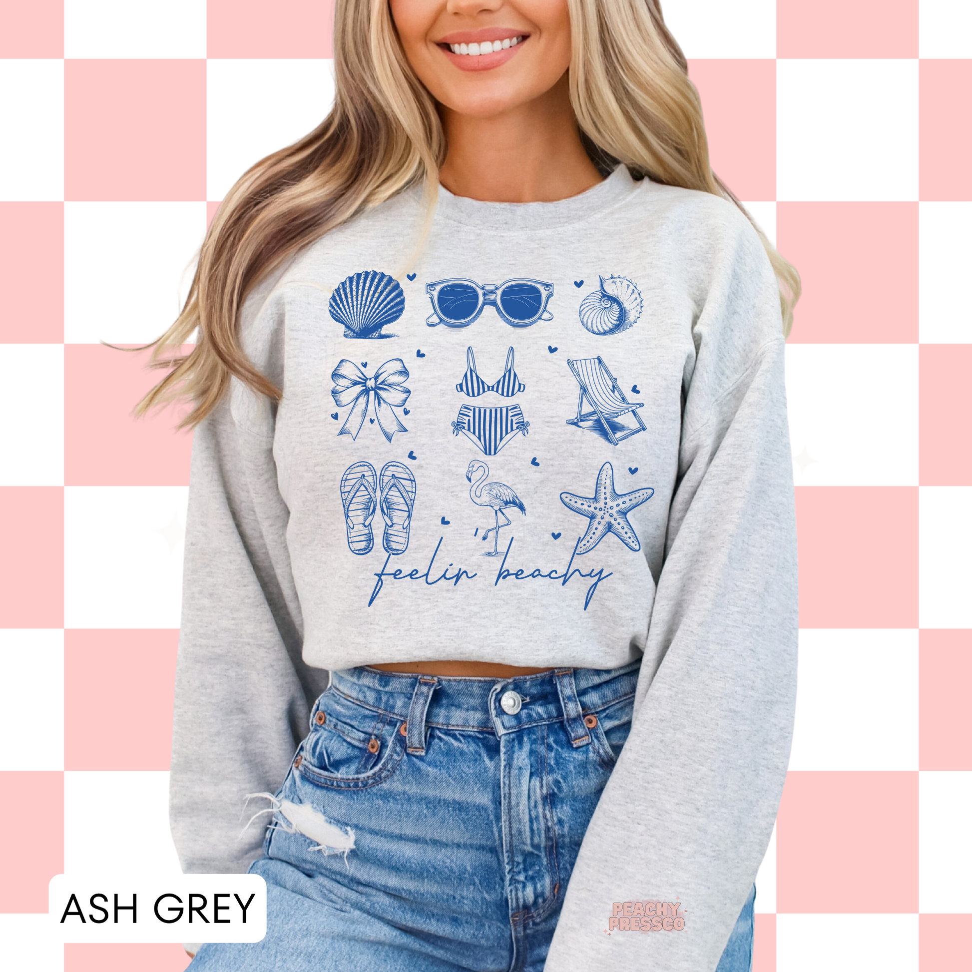 Woman wearing an ash grey sweatshirt with blue beachy doodle graphics including sunglasses, flamingo, seashells, and flip flops.