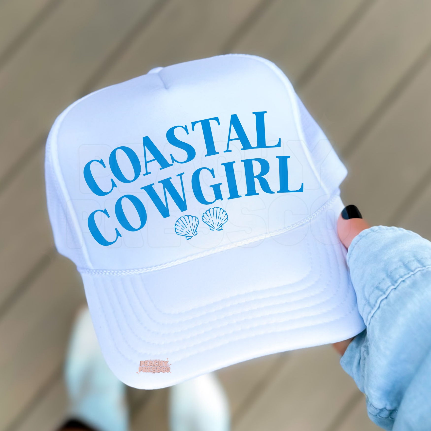 Coastal Cowgirl white trucker hat with blue typography and seashell design for beach vacations and summer fashion.