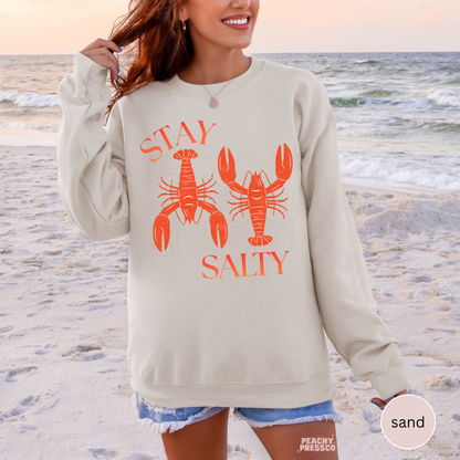 Sand crewneck sweatshirt featuring coral “Stay Salty” lobster graphic – coastal beach sweatshirt for women, summer vacation apparel.