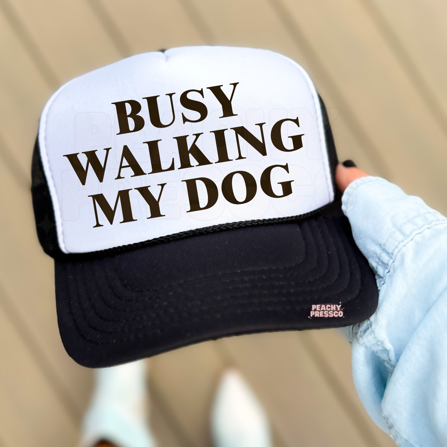White and Black trucker hat featuring “Busy Walking My Dog” text.

