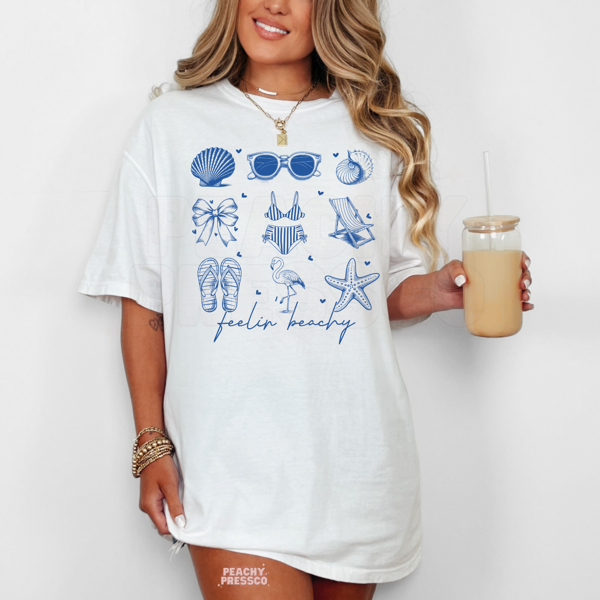 Woman wearing a white oversized graphic t-shirt with blue coastal summer icons and handwritten “feelin beachy” text.