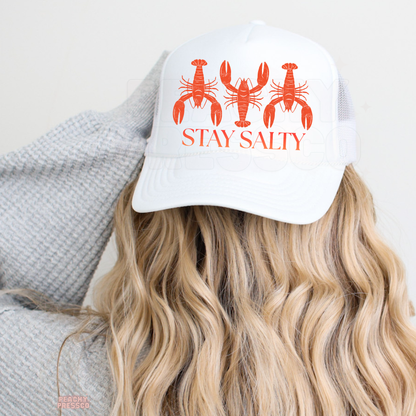 White trucker hat with coral lobster artwork and “Stay Salty” graphic, inspired by coastal living, seaside trips and laid-back summer vibes.