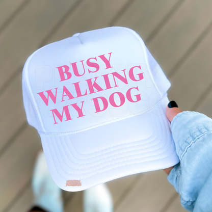 White with Pink trucker hat featuring “Busy Walking My Dog” text.
