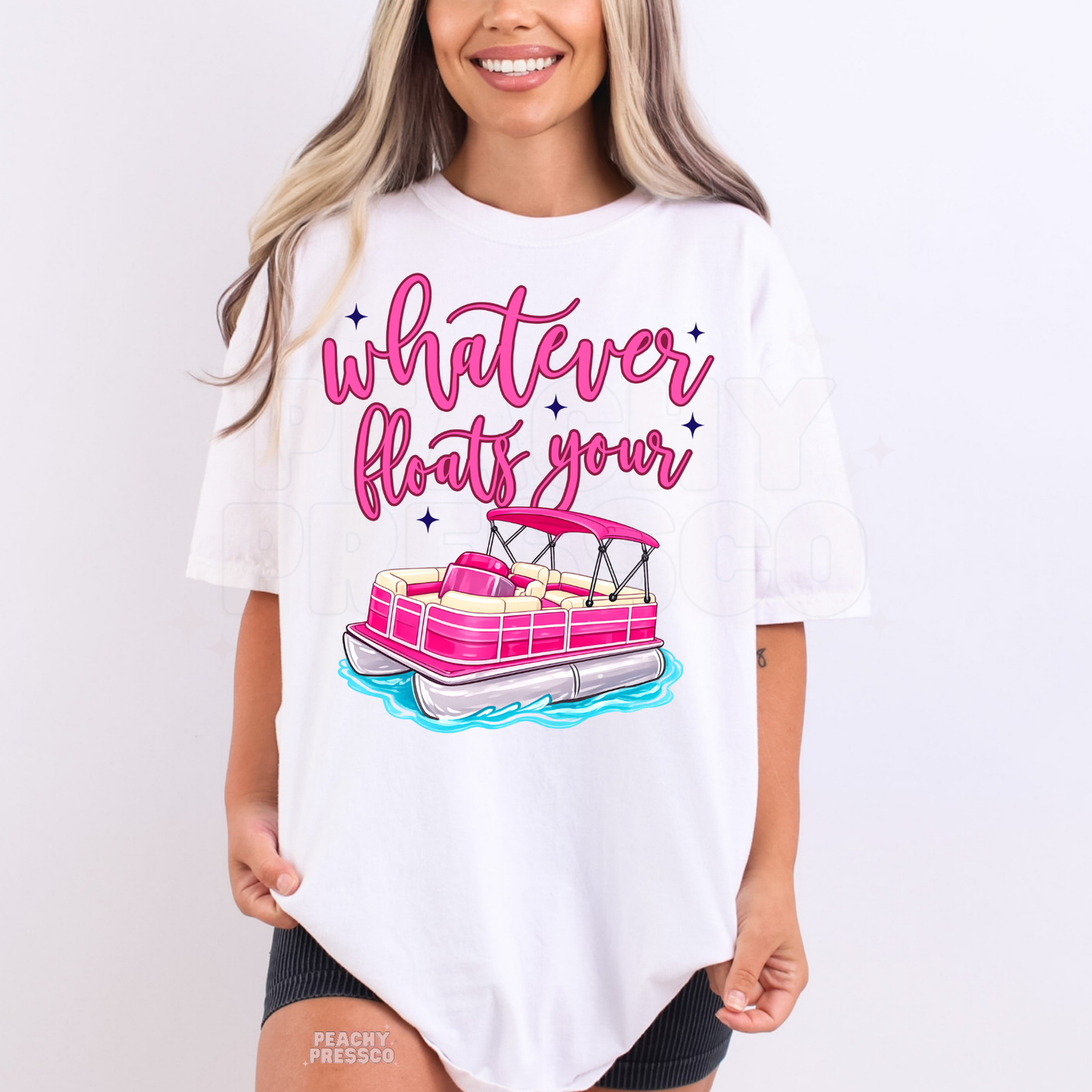 Woman wearing a white graphic t-shirt featuring pink pontoon boat artwork with “Whatever Floats Your Boat” lettering.
