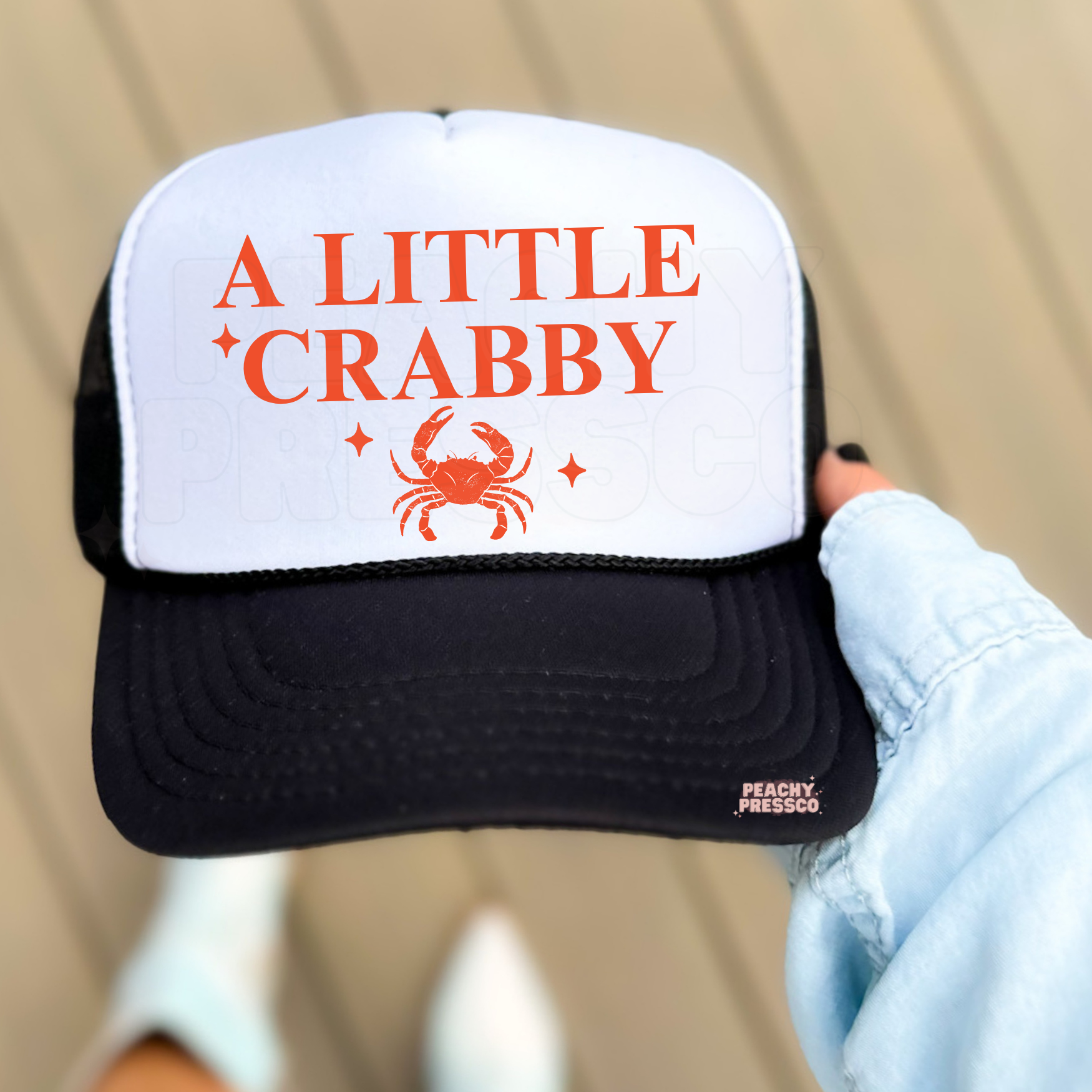 Black and white trucker hat with orange crab graphic and A Little Crabby text.
