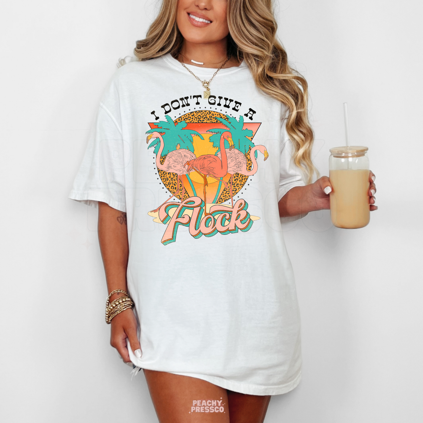 Woman wearing a white oversized flamingo graphic tee with colorful tropical sunset artwork and funny beach quote.