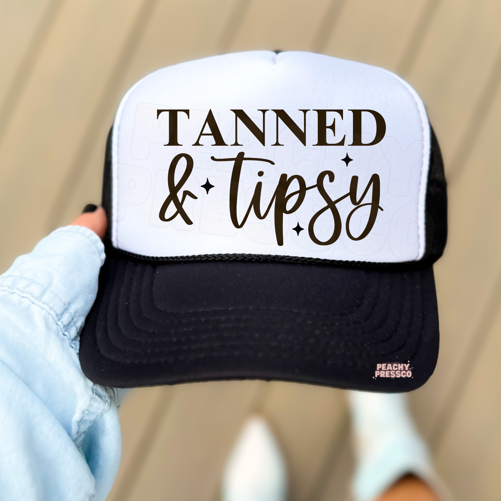 Black and white trucker hat with Tanned and Tipsy lettering.
