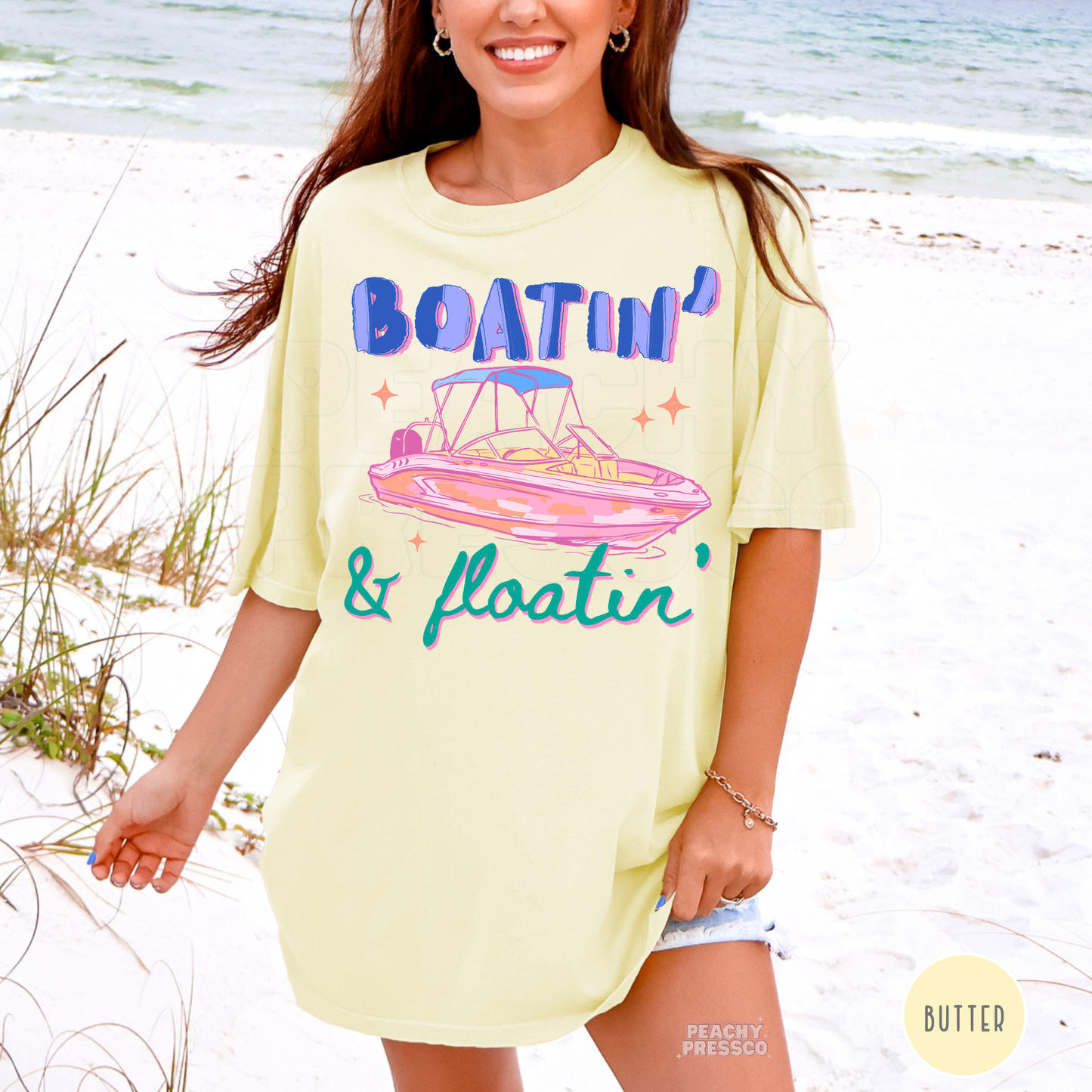 Woman wearing a butter yellow oversized Boatin’ & Floatin’ graphic t-shirt on the beach with colorful retro boat design.