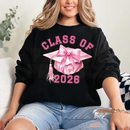 Cute Class of 2026 graduate crewneck with pink bow graduation cap graphic, coquette aesthetic design, and grad year apparel.