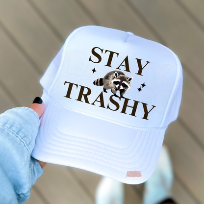 White trucker hat with “Stay Trashy” text and raccoon graphic, funny women’s trucker cap for lake days, camping, casual outfits and outdoor adventures.