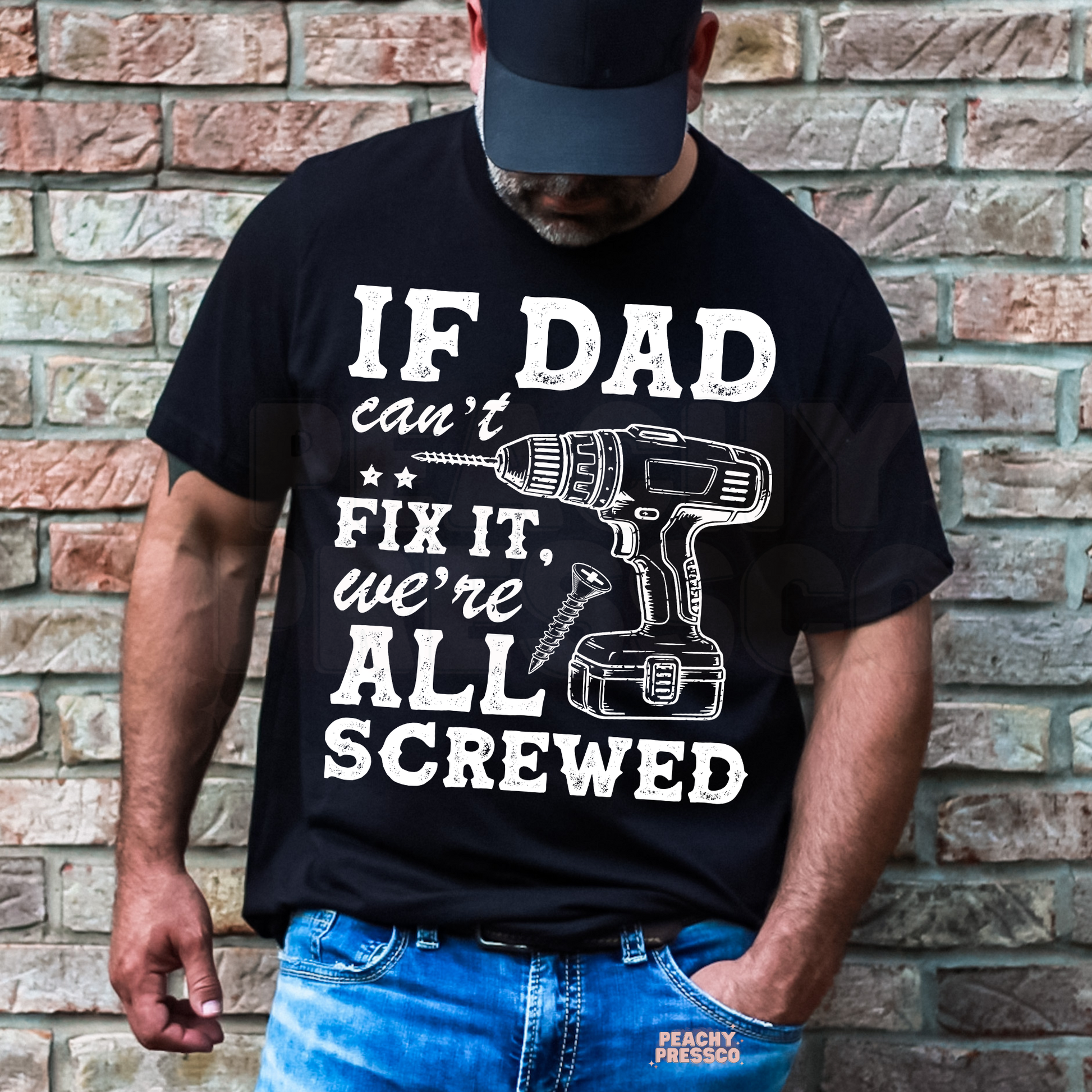 Man wearing black t-shirt with funny “If Dad Can’t Fix It, We’re All Screwed” graphic featuring a power drill illustration.