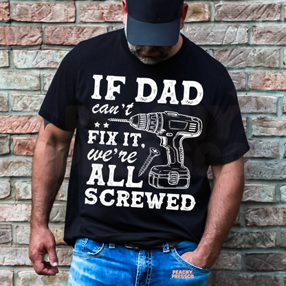 Man wearing black t-shirt with funny “If Dad Can’t Fix It, We’re All Screwed” graphic featuring a power drill illustration.
