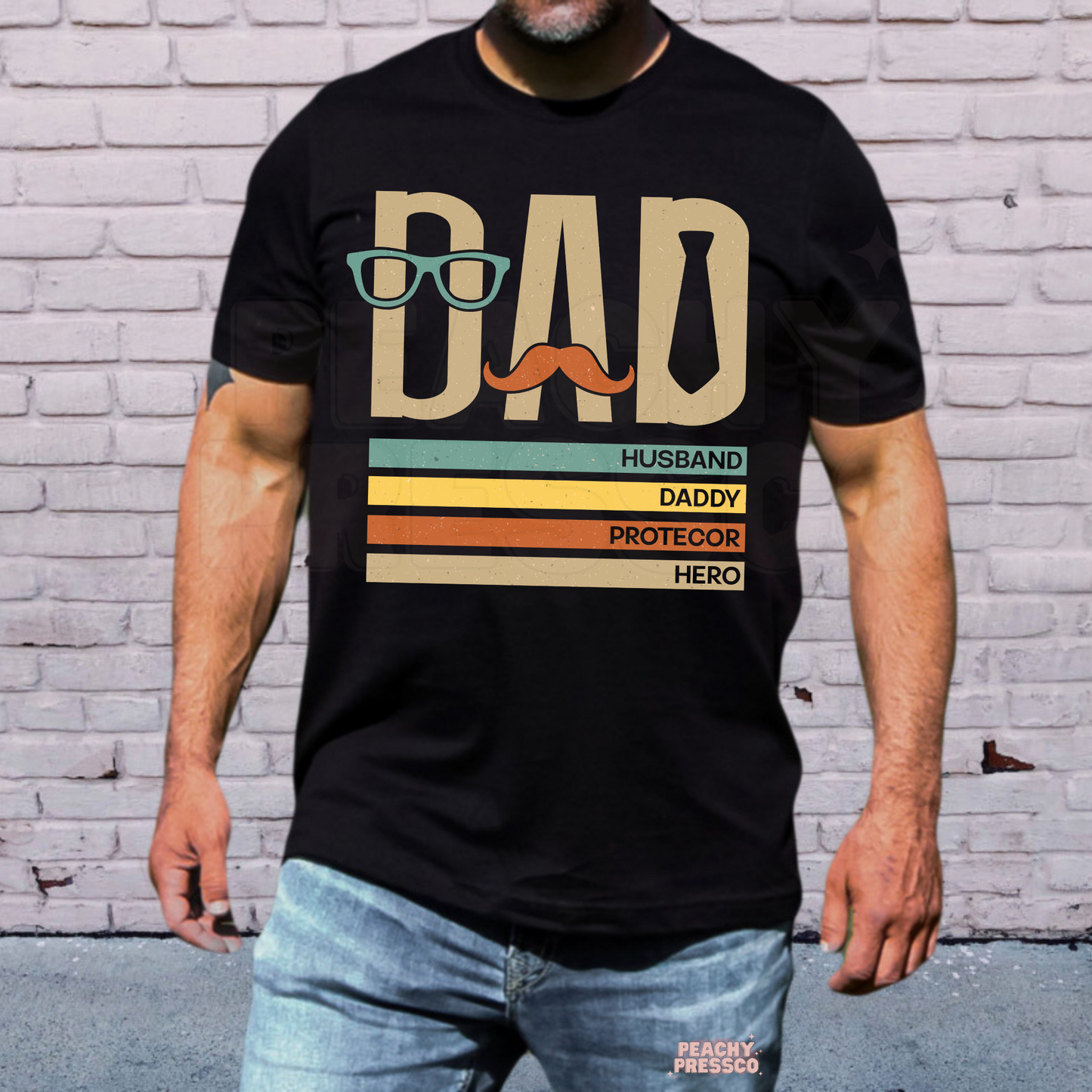 Man wearing black t-shirt with retro “Dad” graphic featuring glasses, mustache, tie, and funny fatherhood text design.