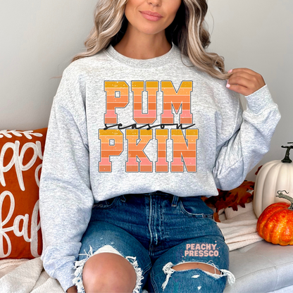 Person wearing a gray sweatshirt with 'PUMPKIN' text, sitting on a couch with pumpkins and fall decorations.