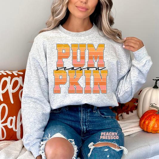 Person wearing a gray sweatshirt with 'PUMPKIN' text, sitting on a couch with pumpkins and fall decorations.