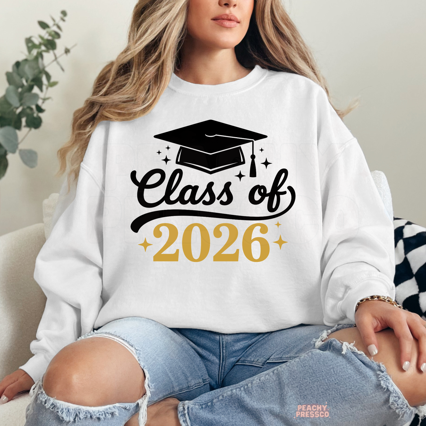 Woman wearing white Class of 2026 graduation sweatshirt featuring black script lettering and graduation cap graphic.